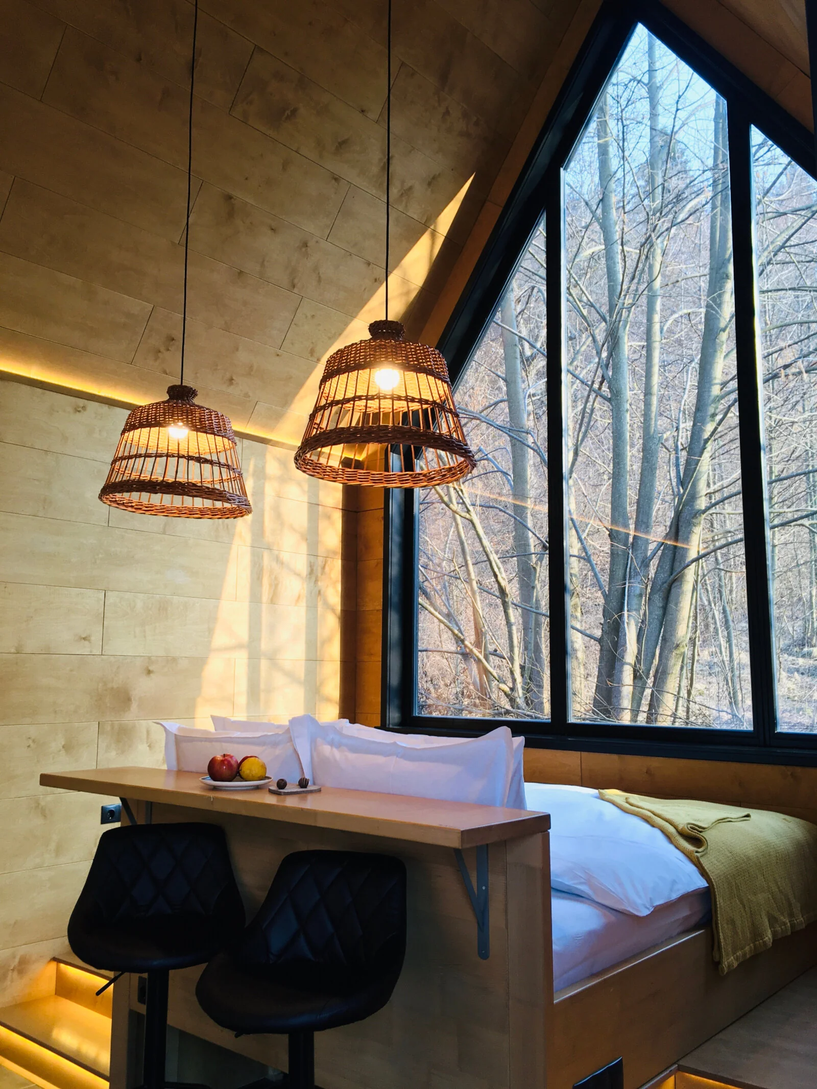 Interior de bungalou cu pat, fereastră spre pădure și lumină caldă